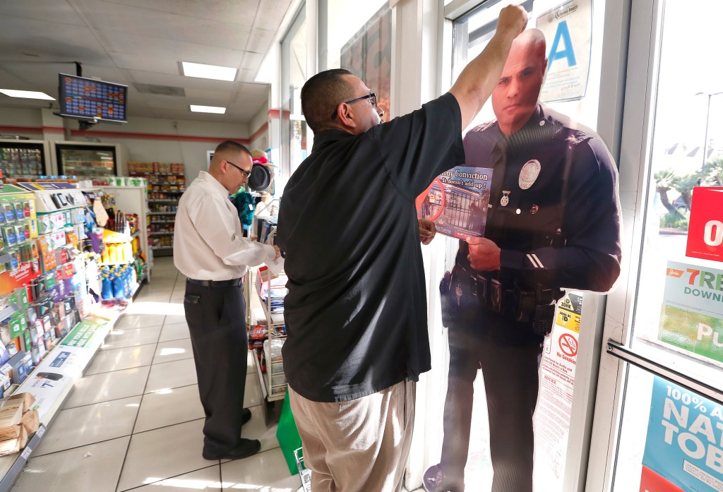 Albert Melena y Bart Trevino, miembros del San Fernando Valley Partnership, colocan posters policiales en una tienda de abarrotes de Mission Hills. /AURELIA VENTURA 