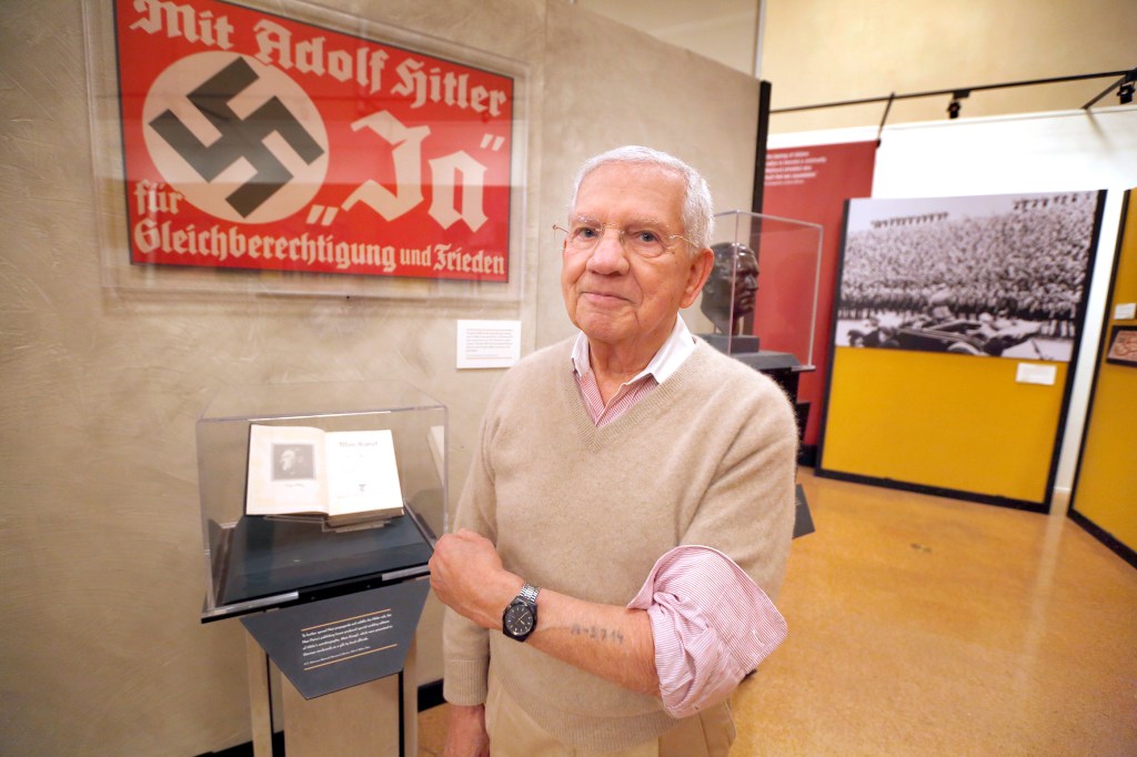 Robert Clary, un sobreviviente del holocausto, posa junto a un afiche Nazi que es parte de la exhibición en la biblioteca. / (Foto: Aurelia Ventura/La Opinion)