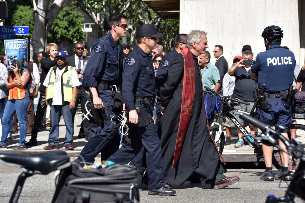 Policías detienen al religioso Chris Ponnet, del Centro Camillus Católico Romano tras una protesta contra las deportaciones, en Los Ángeles, California. 