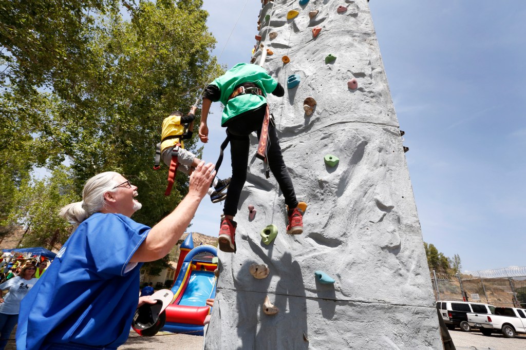 Tony Haschke ayuda a sus nietos Michael López, de 8 años, y Aden, de 7 años, a escalar una roca durante el evento de presos con hijos y nietos. (Foto:Aurelia Ventura/ La Opinion)