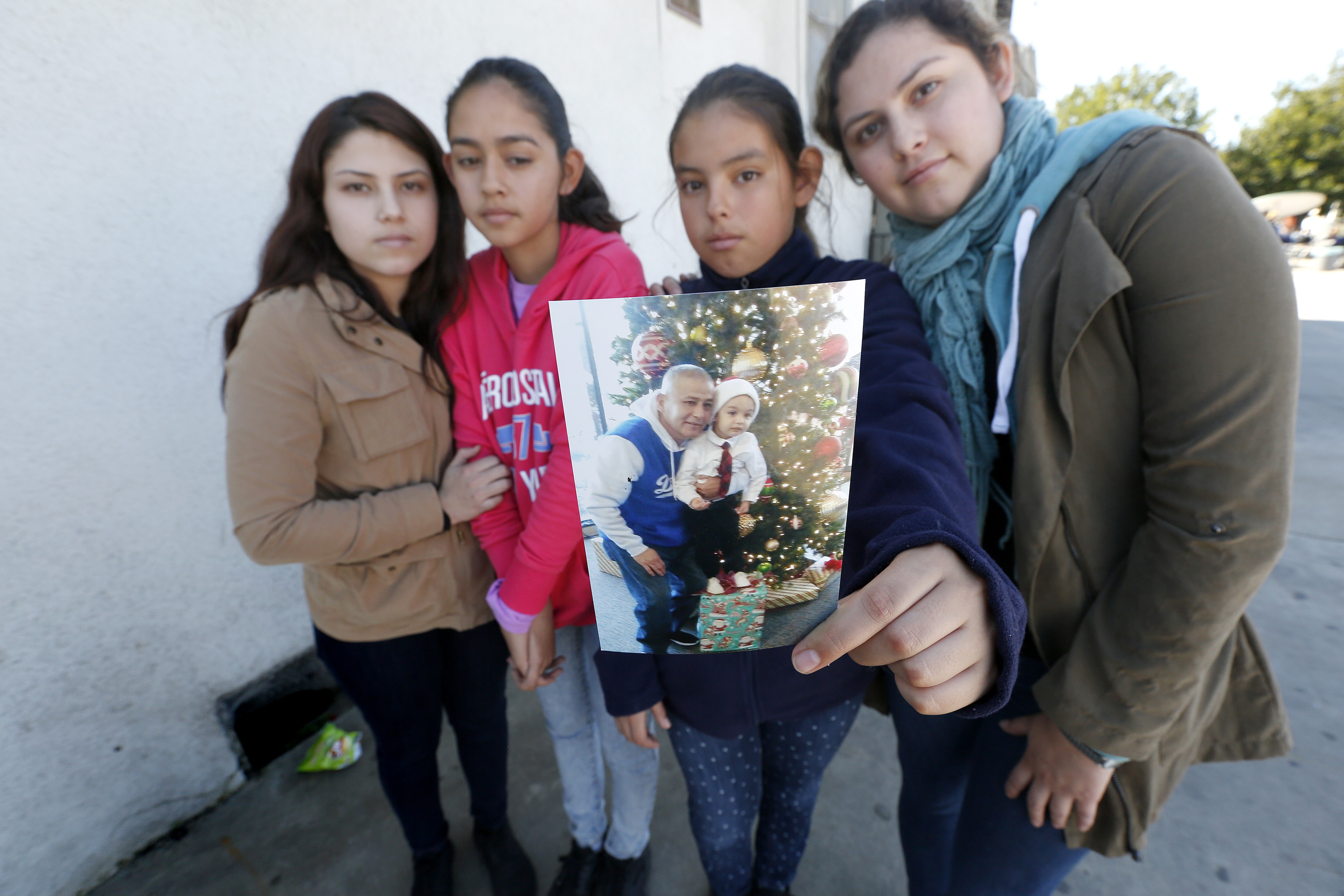 Brenda Avelica, de 24 años, junto a sus hermanas menores, Joselyn, de 19, Fatima de 13, y Yuleni, de 12, muestran una foto de su padre, Romulo Avelica, detenido mientras llevaba a sus hijas a la escuela. (Aurelia Ventura/La Opinion)