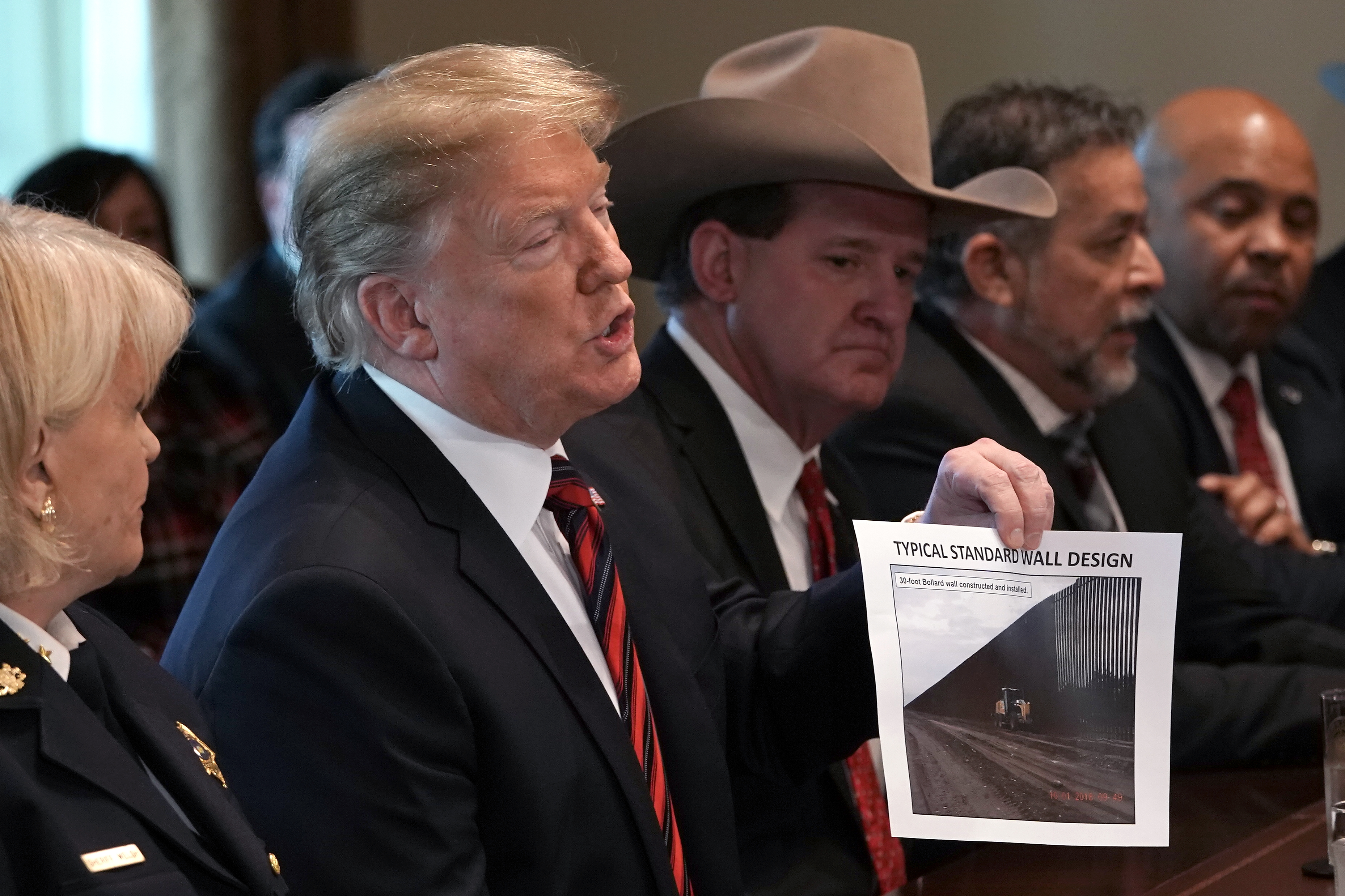 El Presidente Donald Trump sostiene una foto con el escrito "diseño típico estandar del muro" durante una reunión en la Casa Blanca.