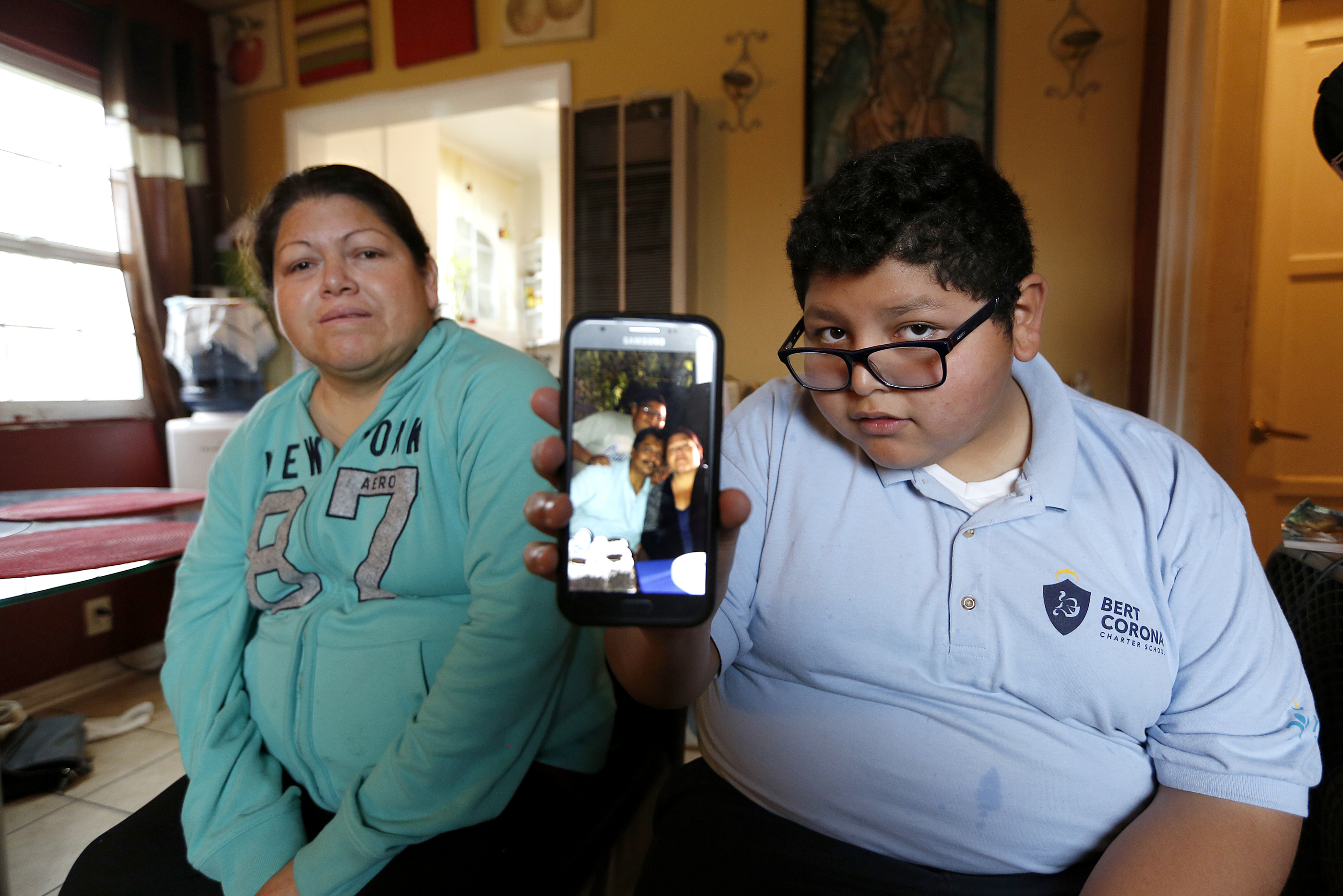 Marisela Hernández y su hijo Juan Pablo Guzman de 12 años muestran una foto del padre, Juan Aquino, detenido por ICE cuando llevaba el menor a la escuela. (Aurelia Ventura/La Opinion)